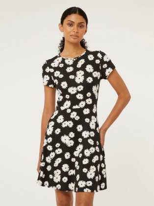 A woman posing in a black and white daisy print dress.
