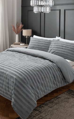 A grey duvet set on a double bed beside a bedside table topped with a vase and lamp.