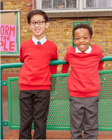 Two boys leaning against a railing wearing red school jumpers and trousers.