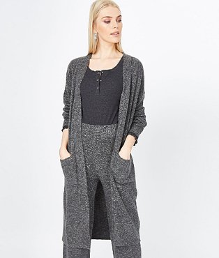 A woman wearing a charcoal open front longline cardigan over a black top, matching charcoal trousers and white trainers.