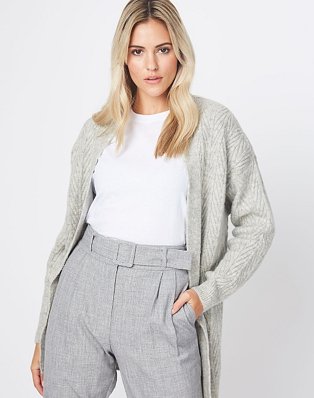 A woman wearing a grey chevron knit cardigan over a white t-shirt and grey tailored trousers.