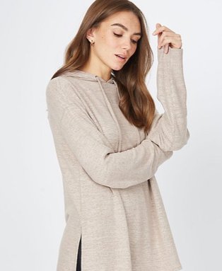 Woman poses side on resting elbow on arm wearing stone marl woven side slit hoodie.