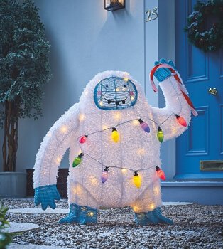 White Christmas waving Yeti light outside on grey pebbles with blue door in the background. 