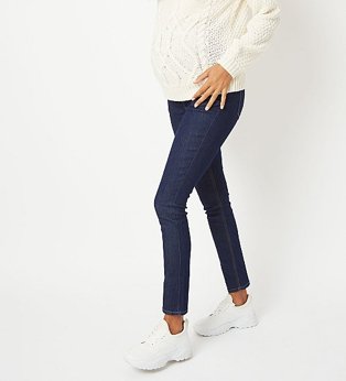 Woman wearing a cream chunky knit jumper with blue maternity jeans, and white sneakers