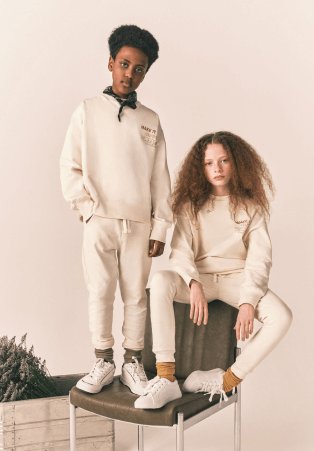 A girl and boy wearing cream unisex joggers and hoodie sets.