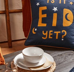 An Eid slogan cushion and gold-accented crockery on a table