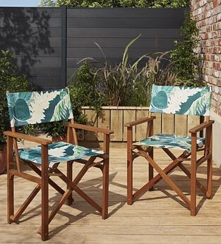 Two wooden chairs with green leaf patterned fabric