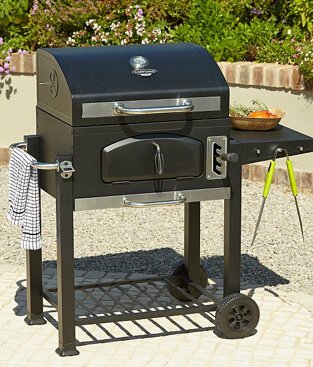 Classic amercian style charcoal grill on an outdoor patio, with tongs and a tea towel hanging on the side