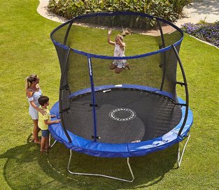 One child bouncing on a large trampoline with safety enclosure with two children watching from the side