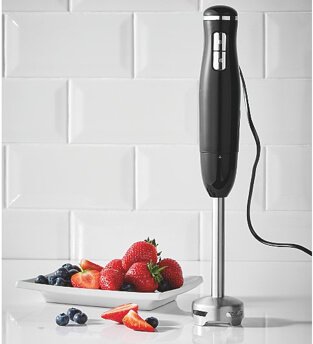 Stick blender standing upright next to a plate of berries