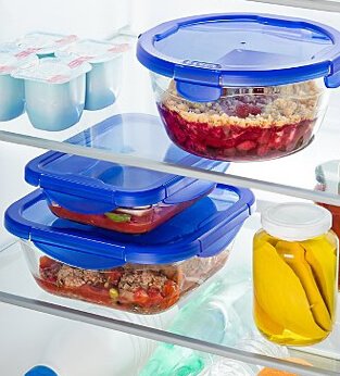 Reusable glass food containers with blue snap lids sitting on fridge shelves