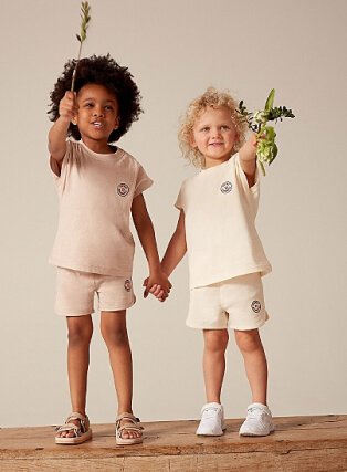Two children holding hands wearing cream and pale pink t-shirt and shorts set.