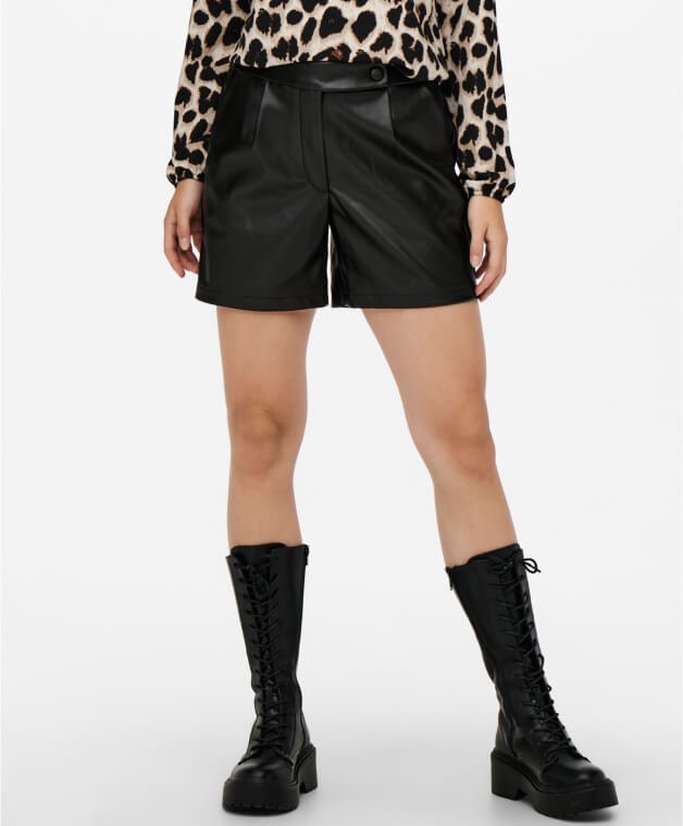 A waist down shot of a woman posing in JDY black faux leather shorts, chunky black boots and an animal print top.
