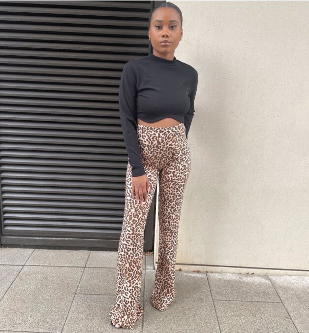 A woman posing in G21 leopard print flared trousers and black long sleeve top.
