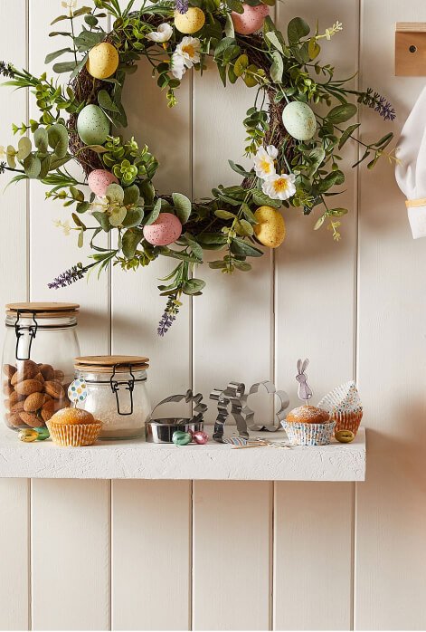 An Easter wreath with pastel egg decorations hanging on a wooden wall