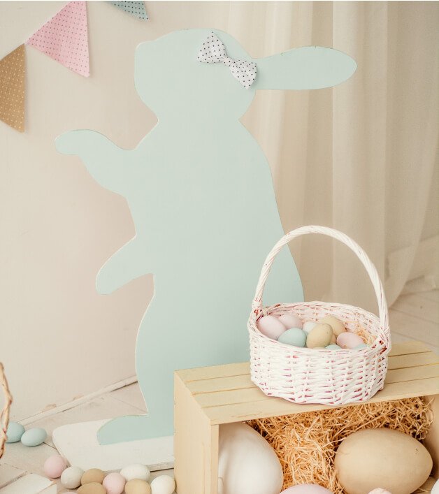 A white Easter basket filled with eggs in front of a pastel bunny decoration