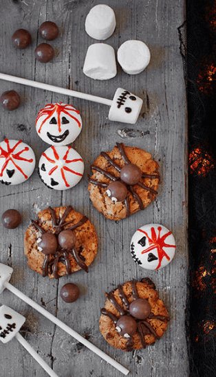 A wooden table topped with a selection of Halloween sweet treats including cookies, marshmallows and meringues.