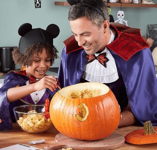 A father and son carving a pumpkin in matching vampire costumes.