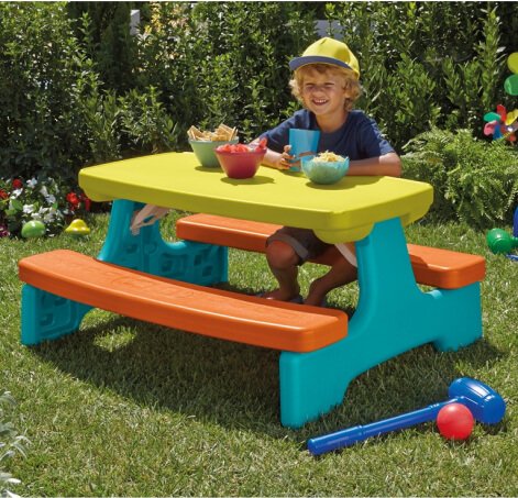 Child sits on colourful table playing with toys.