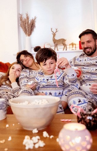 A family eating popcorn on a sofa in matching festive pyjamas