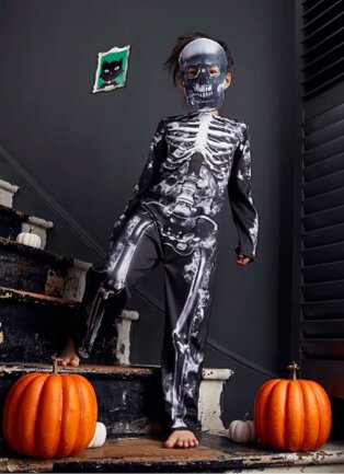 Child wearing halloween skeleton black and white halloween costume, with one pumpkin either side of him.