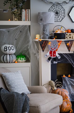 A living room decorated with halloween bunting, painted pumpkins, spiderwebs and toy spiders, fake candles and cauldrons full of sweets