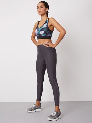 Woman stood wearing a blue and black patterned sports bra and grey gym leggings with grey trainers