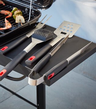 A BBQ side tray with an assortment of BBQ utensils, including a spatula and tongs