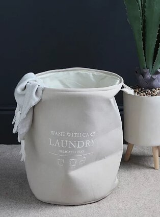 Light grey slogan laundry basket with artificial plant in the background.