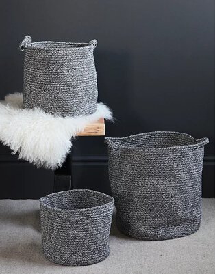 Medium grey storage basket on wooden seat and white faux fur rug with coordinating small and large baskets on the floor.