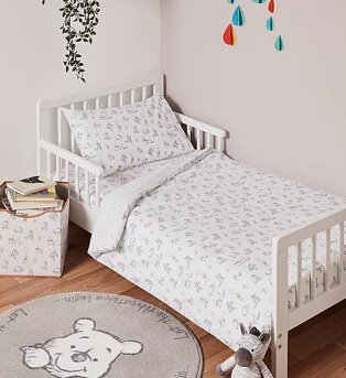 Kids bedroom features white cot bed with Disney Winnie the Pooh print duvet set with matching round rug and storage box.