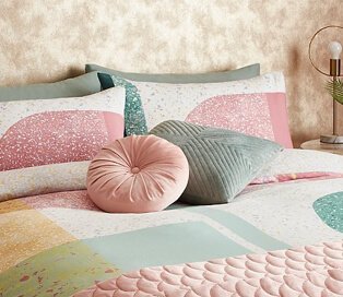Double bed with multi-coloured pastel pattern with pink and green decorative cushions and pink quilted throw