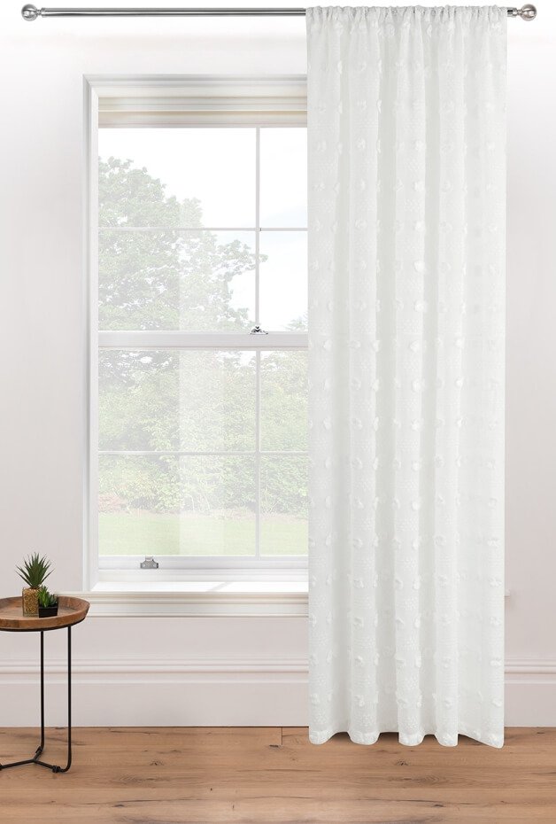 A small side table next to a window with white floor length curtains.