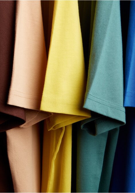A close shot of brightly coloured t-shirts on hangers.