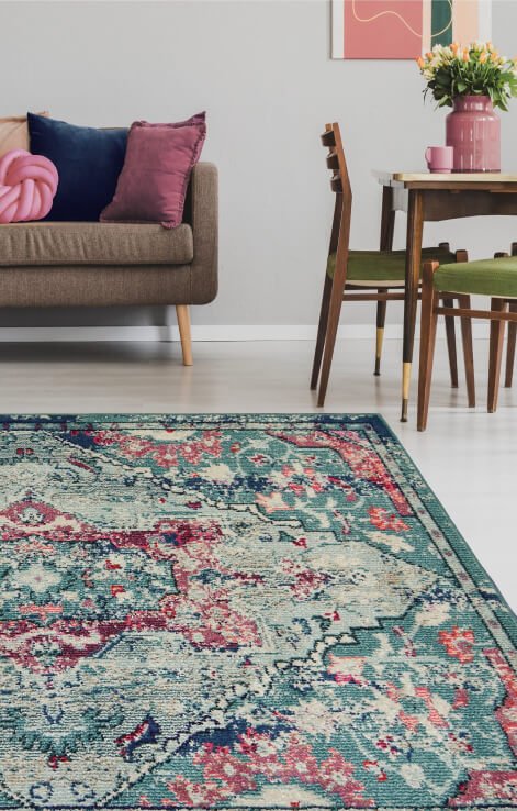 A green patterned rug in front of a sofa and dining table and chairs set.