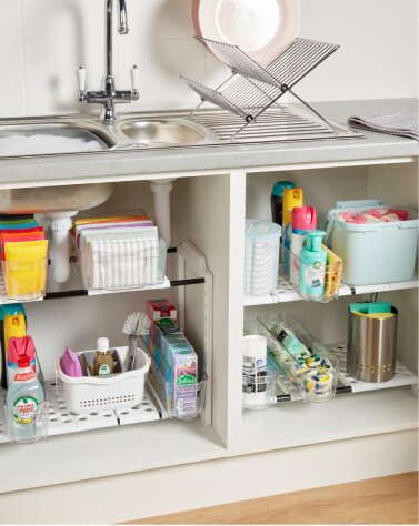 A kitchen sink cupboard with cleaning products in various sized organisers.