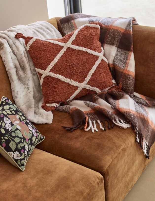 A tan sofa with tonal throws and cushions.