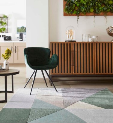 A green velvet chair on a green, grey and white geometric rug.