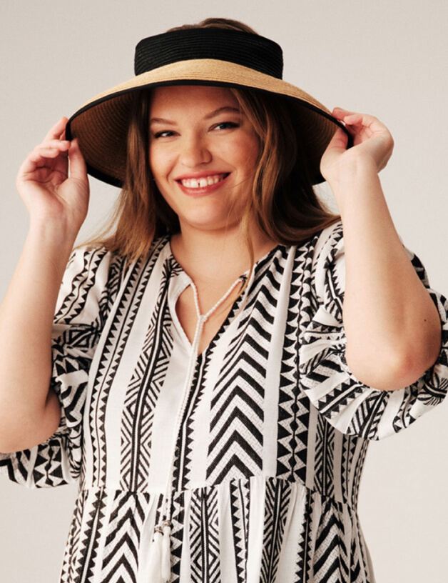 A woman wearing a monochrome patterned dress and a straw hat.