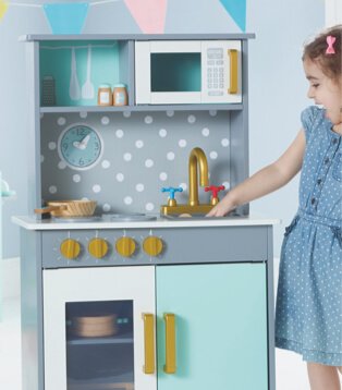 Girl wearing blue dress smiles standing next to wooden deluxe kitchen.