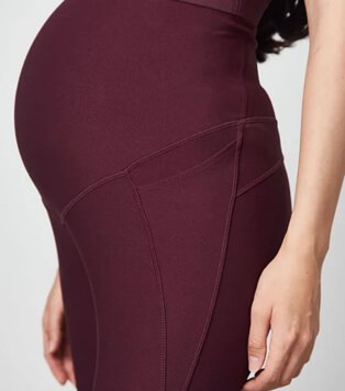 A close shot of a pregnant woman wearing maternity plum sports leggings.