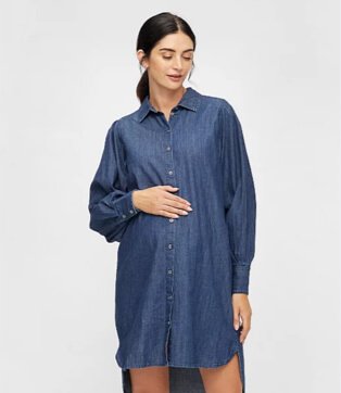 A pregnant woman standing with her hand on her bump wearing a Pieces denim shirt dress.