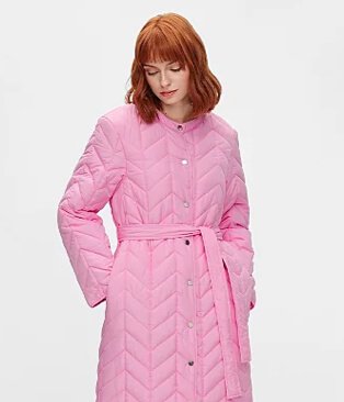 Woman poses with hands in pockets wearing pink padded longline belted coat.