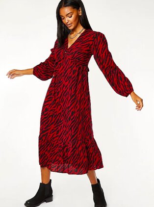 Woman poses wearing red and black animal print dress and black ankle boots.