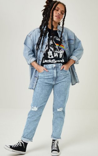 Woman poses with hands in pockets wearing light blue distressed jeans, black Pink Floyd t-shirt, denim jacket and black lace-up pumps.