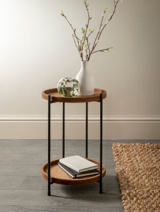 2-tiered round wooden table features white vase with artificial flowers, glass ornament and stack of books.