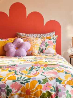 Vibrant floral bedding topped with pink flower-shaped cushion.