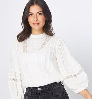 A woman wearing a cream ladder insert embroidered blouse with black jeans.