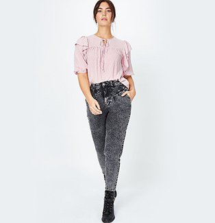 A woman wearing a pink bobble texture frill detail blouse with black acid wash jeans and black boots.