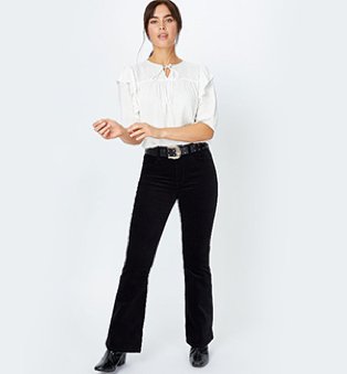 A woman wearing a white bobble texture frill detail blouse with black jeans and boots.